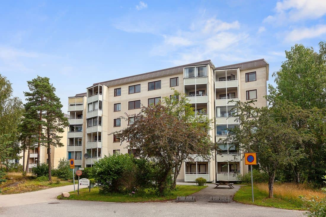 BRF Melodins hus med inglasade balkonger omgivet av grönska en solig dag